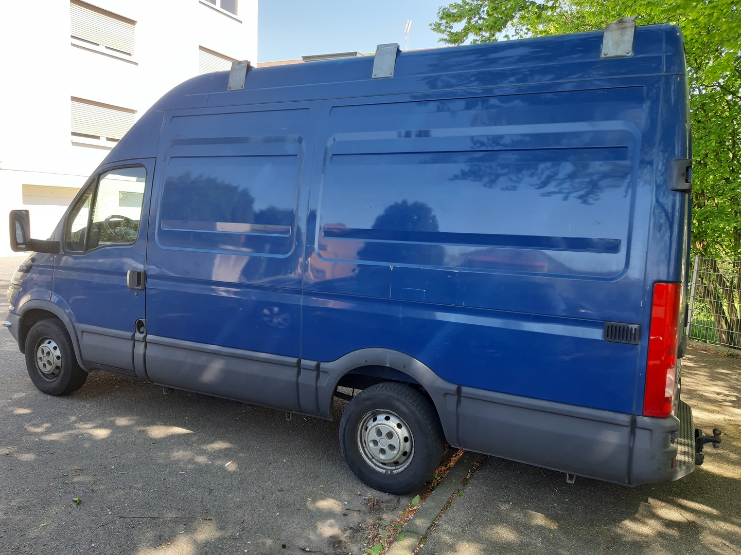 Ein blauer Lieferwagen steht auf einem Parkplatz vor einem Gebäude.